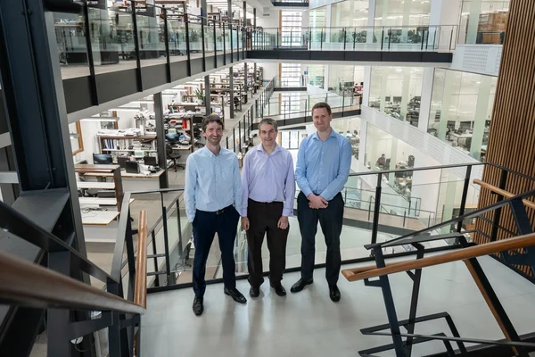 Trois hommes en tenue professionnelle décontractée dans un immeuble de bureaux moderne.