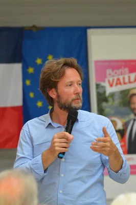 Boris Vallaud prenant la parole devant les drapeaux français et européen.