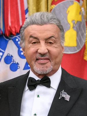 Sylvester Stallone en smoking devant des drapeaux