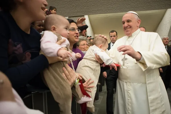 Le pape François souriant en interaction avec des familles lors d'une audience au Vatican.