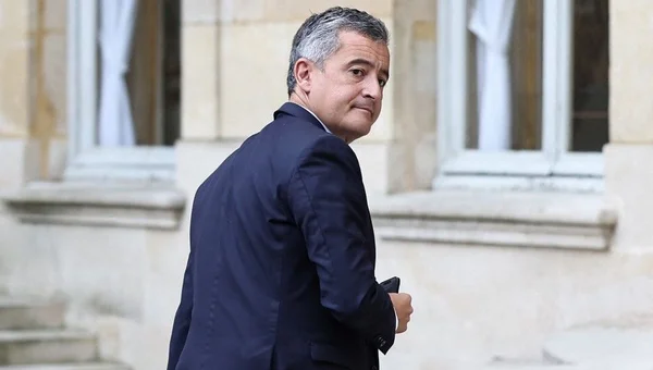 Gérald Darmanin marchant devant un bâtiment en pierre.
