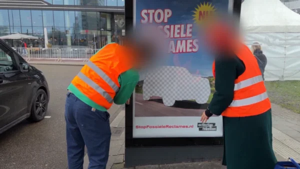 Militants recouvrant une publicité pour voiture d'un autocollant 'STOP FOSSIELE RECLAMES' à Amsterdam.