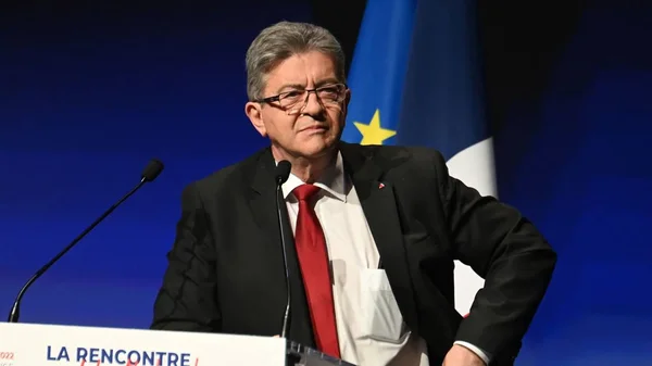 Jean-Luc Mélenchon derrière un pupitre, devant les drapeaux français et européen.