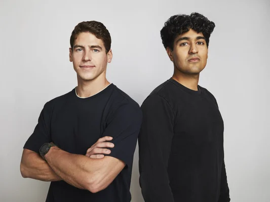 Deux hommes en chemise noire posent dos à dos sur fond blanc pour un portrait lié à Shinkei Systems.