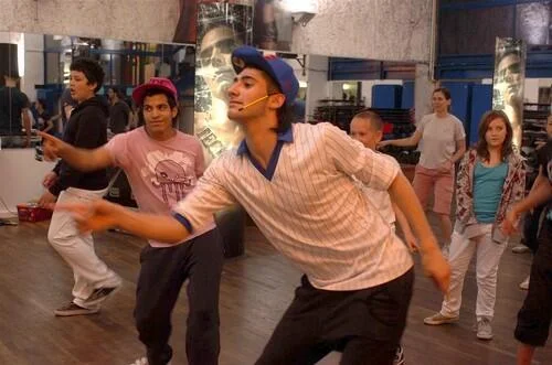 Répétition de danse Tecktonik dans un studio parisien, avec un danseur en casquette bleue menant le groupe.