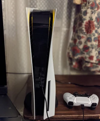 Console PlayStation 5 positionnée verticalement avec le socle et la manette DualSense en charge.