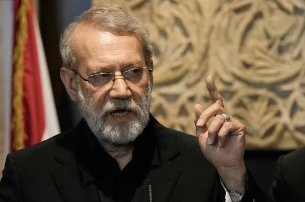 Ali Larijani s'exprimant lors d'une intervention, avec un drapeau en arrière-plan.