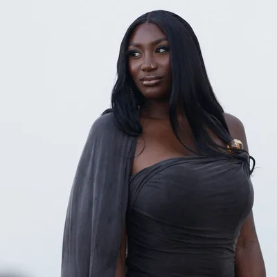 Aya Nakamura en robe grise et broche dorée, fond blanc.