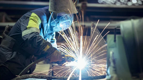 Soudeur au travail dans une aciérie, avec gerbe d'étincelles.