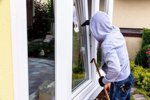Un cambrioleur force une fenêtre à l'aide d'un pied-de-biche, scène typique d'un home-jacking.