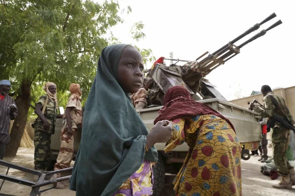 Une jeune fille près d'un camion militaire équipé d'un canon antiaérien, avec des soldats en arrière-plan.