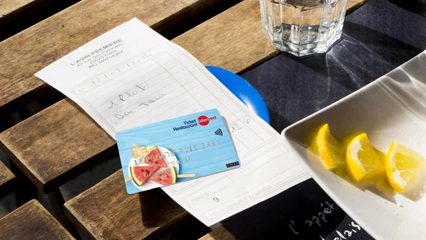 Carte Ticket Restaurant sur un reçu de restaurant, avec verre d'eau et citrons.