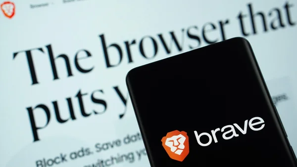 Smartphone affichant le logo Brave devant un écran d'ordinateur avec du texte promotionnel.
