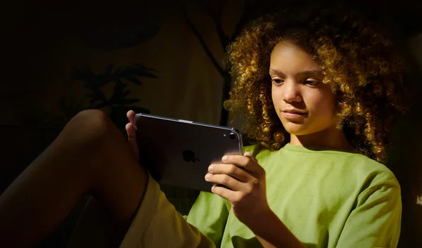 Un enfant utilise un iPad dans une pièce sombre, illustrant l'usage des écrans.
