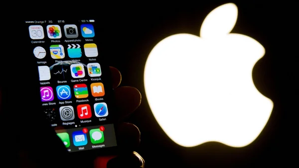 iPhone avec écran d'accueil français près d'un logo Apple lumineux.