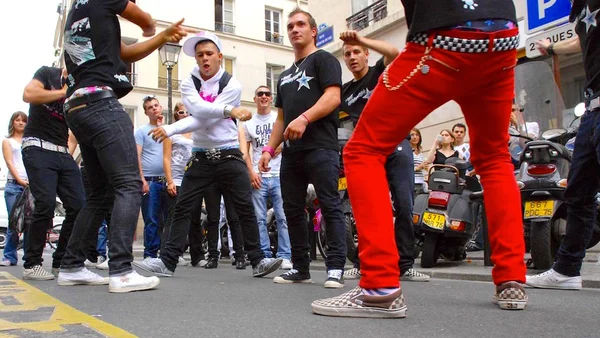 Danseurs Tecktonik en pleine performance de rue, vêtus de streetwear, avec des spectateurs et scooters en arrière-plan.