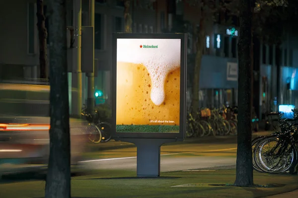 Publicité Heineken illuminée dans une rue animée la nuit.