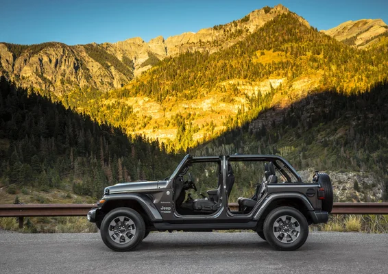 Vue de profil d’un Jeep Wrangler gris foncé décapoté, stationné sur une route devant un paysage montagneux.