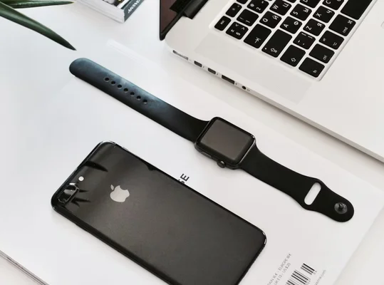 iPhone noir, Apple Watch noire et ordinateur portable argenté sur fond blanc avec une feuille verte.