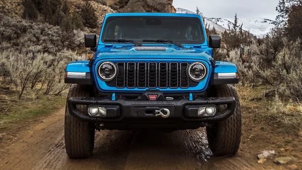 Un Jeep Wrangler Rubicon bleu vif en action sur un sentier boueux en montagne.
