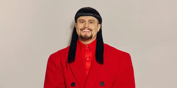 Portrait promotionnel d'Oliver Tree, vêtu de rouge, souriant devant un fond uni.