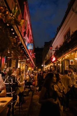 Ambiance de soirée parisienne dans une rue étroite illuminée de guirlandes et de lumières chaudes.