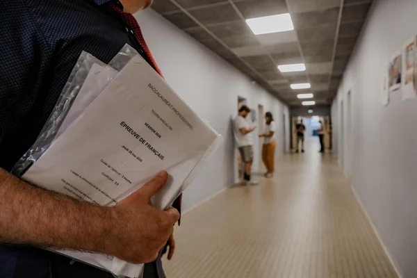 Un élève tenant sa copie d'examen du bac de français professionnel dans un couloir d'établissement.