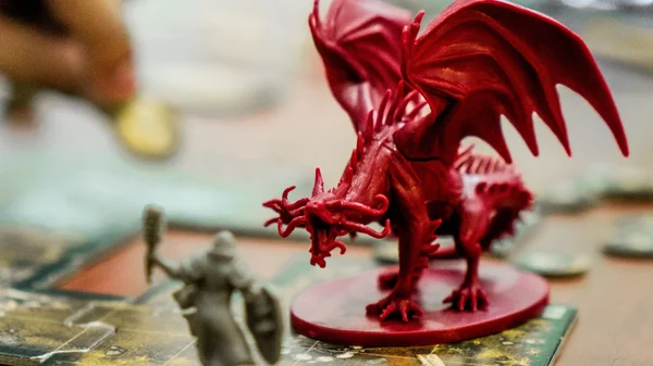 Figurines de jeu représentant un dragon rouge et un guerrier sur un plateau.