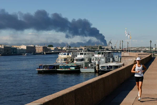Une joggeuse longe la rivière à Saint-Pétersbourg alors que la fumée de l'attaque du terminal pétrolier s'élève en arrière-plan.