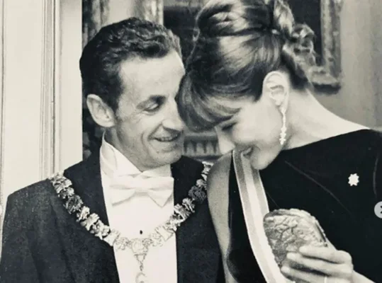 Nicolas Sarkozy en tenue officielle souriant à Carla Bruni qui regarde un objet.