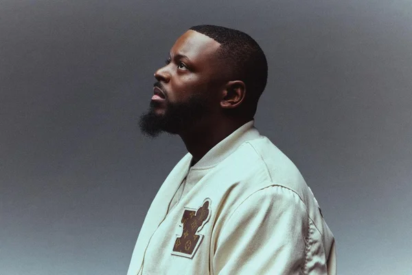 KeBlack en portrait de profil, veste bomber beige.
