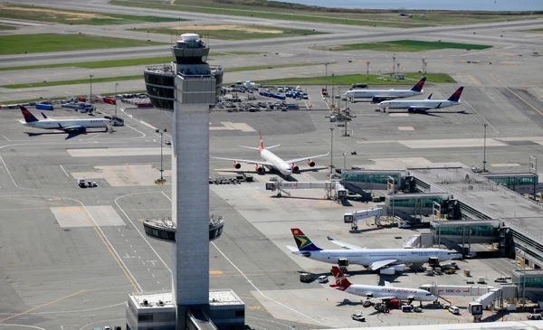 Vue aérienne du tarmac de l'aéroport JFK avec sa tour de contrôle et plusieurs avions.