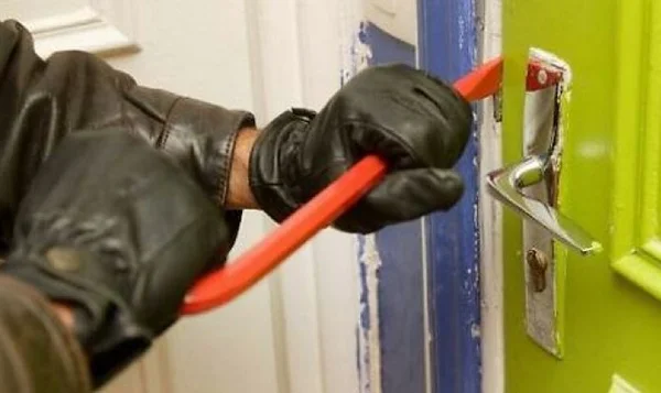Un individu force une porte d'entrée avec un pied-de-biche, méthode courante lors des home-jackings.