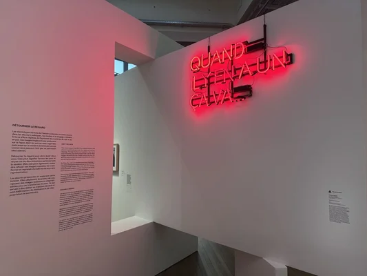 Vue de l'exposition « Aux origines » : un néon rouge et un texte explicatif sur les discriminations.