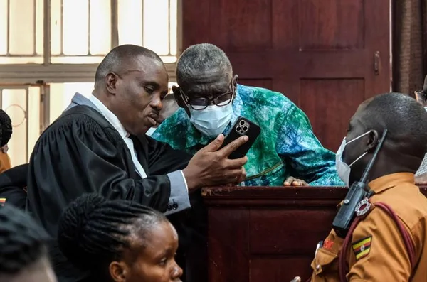 Un avocat présente un téléphone à un homme âgé lors d'une audience au tribunal en Ouganda.