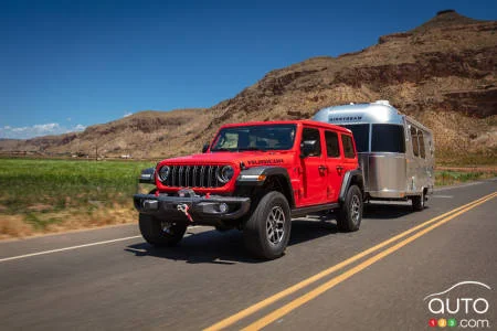 Jeep Wrangler Rubicon rouge remorquant une caravane Airstream sur une route dans un paysage aride.