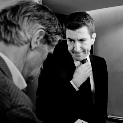 Matthieu Pigasse ajustant son col, vu de profil, dans une scène en noir et blanc.