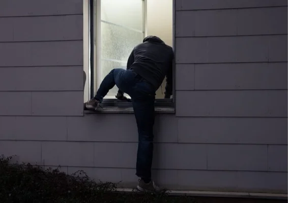 Un individu s'introduit par une fenêtre, illustrant la méthode d'entrée lors d'un home-jacking.