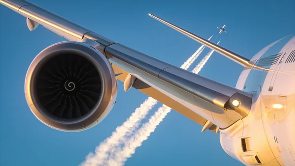 Plan large d'un avion de ligne en vol dans un ciel bleu, aile et réacteur visibles, traînée blanche derrière, lumière du soleil matinal