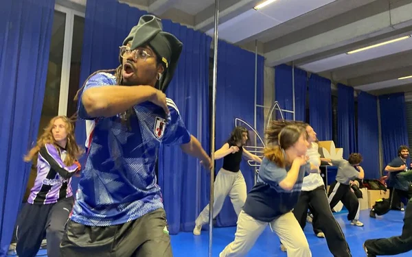 Cours de danse Tecktonik dans un studio bleu, animé par un danseur en maillot de foot et chapeau.