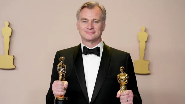 Christopher Nolan avec deux Oscars devant un mur décoré.