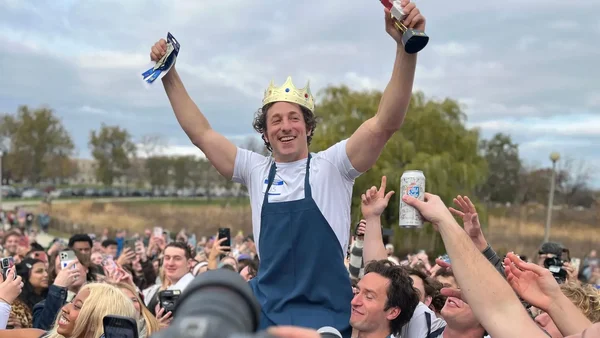 Un participant au concours de sosies célèbre sa victoire, couronné et acclamé par la foule.