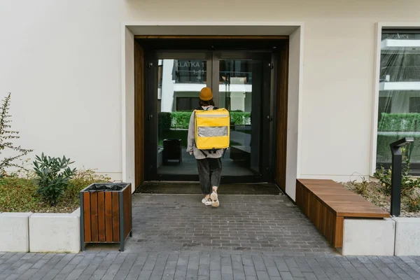 Livreur de repas avec un sac thermique jaune devant un immeuble moderne.