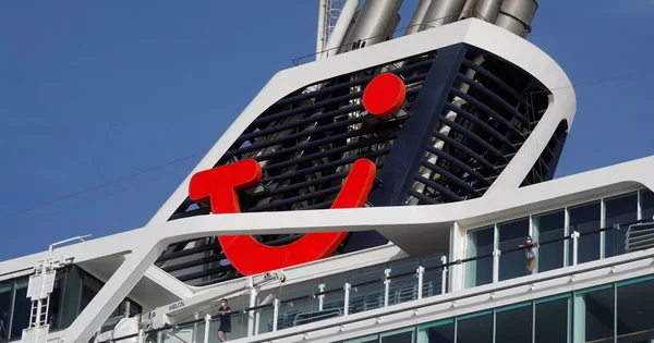 Détail de la cheminée du navire TUI Cruises avec le logo rouge caractéristique, vu en contre-plongée sous un ciel bleu.