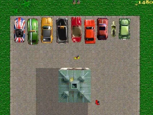 A top-down screenshot from the video game Grand Theft Auto: London 1969. The image displays a lineup of various cars, including one with a Union Jack paint job, parked on an asphalt surface next to a grassy area. A small character and a building are also visible.