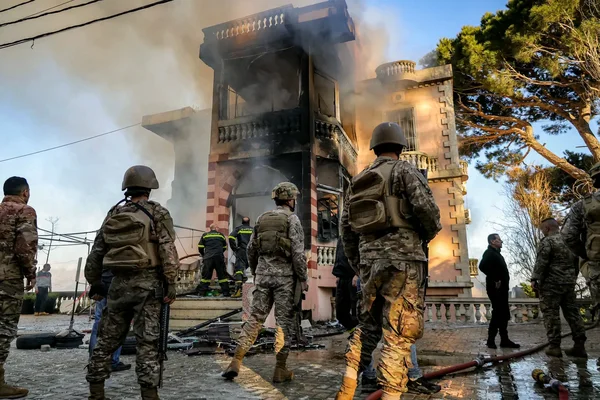 Soldats libanais observant un bâtiment en feu, avec des pompiers en intervention.