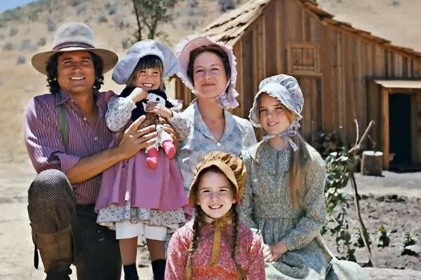 Scène de la série originale La Petite Maison dans la prairie avec la famille Ingalls devant leur cabane.