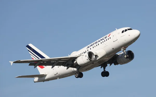 Un Airbus A320 d'Air France en vol, train d'atterrissage sorti, sous un ciel bleu.
