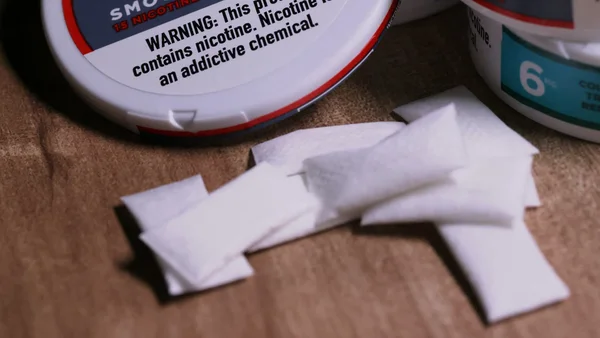 Sachets de nicotine blancs dispersés sur une surface en bois près de boîtes avec avertissement sanitaire.