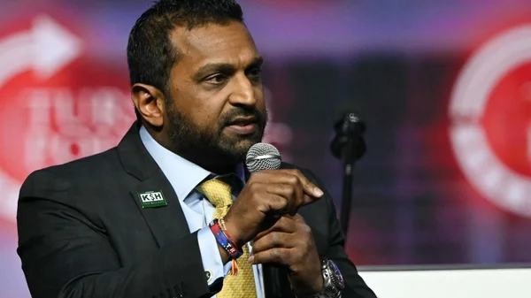 Kash Patel s'exprimant lors d'une conférence, arborant un pin's 'KSH'.